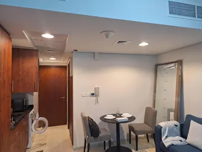 a living room with a table and chairs and a kitchen at Bright Studio Unit at Lake Terrace with lake view in Dubai