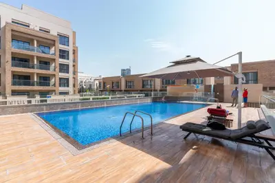 a swimming pool with an umbrella next to a building at Ahlan HH - Stunning Studio in Eleganz 2 Danube, JVC in Dubai