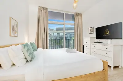 a white bedroom with a large bed and a window at Ahlan HH - Beautiful 1BR Home with Pool View - Belgravia III, JVC in Dubai