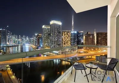 a balcony with two chairs and a city skyline at night at Stylish Renovated 1-Bedroom in Mayfair Residency in Dubai