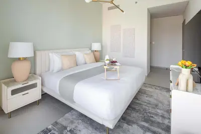 a white bedroom with a large bed and a table at Frank Porter - Grande Signature Residence in Dubai