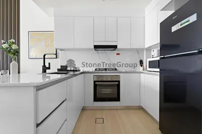 a white kitchen with white cabinets and a black oven at High-Floor and Spacious 1BR at Binghatti Emerald in Dubai