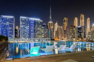 a pool with chairs and a city skyline at night at Luxury Apartment with Burj Khalifa View, Balcony Netflix WeHome Premium in Dubai