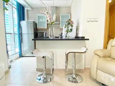 a kitchen with a counter with a refrigerator and two stools at Cozy Studio at Marina near Beach and Metro in Marina Z817 in Dubai