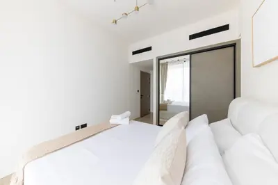 a white bedroom with two beds and a mirror at Bright 1BR with balcony in Binghatti Corner in Dubai