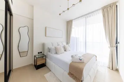 a white bedroom with a white bed and a window at Bright 1BR with balcony in Binghatti Corner in Dubai