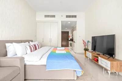 a bedroom with a large bed and a flat screen tv at Luxury Studio in DAMAC Hills with Premium Amenities in Dubai