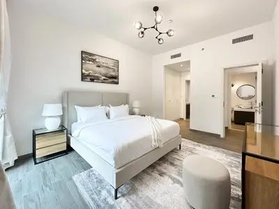 a white bedroom with a bed and a chair at Super Spacious 2BR with Designer Touch in Dubai