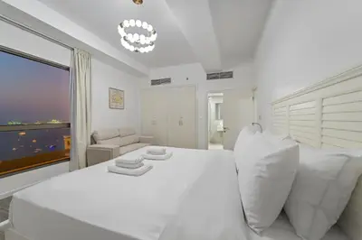 a white bedroom with a large white bed and a window at Elegant 2BR with Seaview in JBR l Walk to the Beach in Dubai