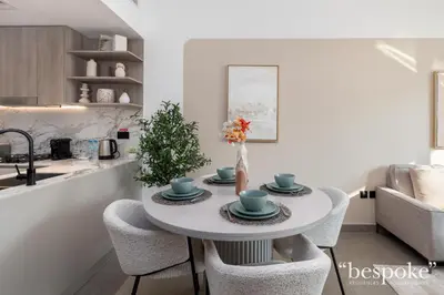 a white kitchen with a table and chairs at Bespoke Holiday Homes - Stylish 1-BR Apartment in Oxford Terraces, JVC in Dubai