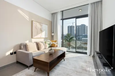 a living room with a couch and a large window at Bespoke Holiday Homes - Stylish 1-BR Apartment in Oxford Terraces, JVC in Dubai