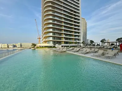 a swimming pool with chairs and a tall building at Seaview Living 2 Bedroom - Grand Bleu by Elie Saab in Dubai