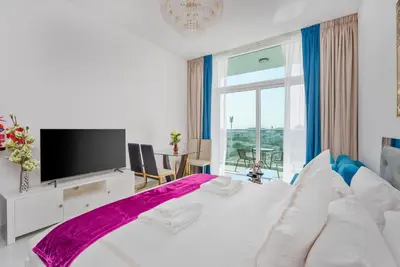 a white bedroom with a large white bed with a tv at Vacay Lettings - Pearlz By Danube -Studio-Al Furjan-Near Metro in Dubai