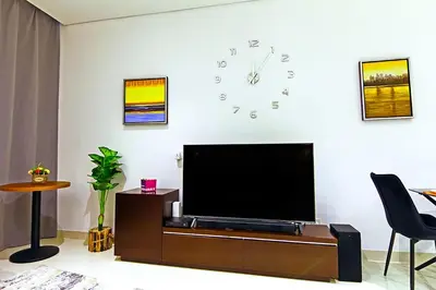 a living room with a television and a clock on the wall at Luxurious 1bhk in Cour Jardin in Dubai
