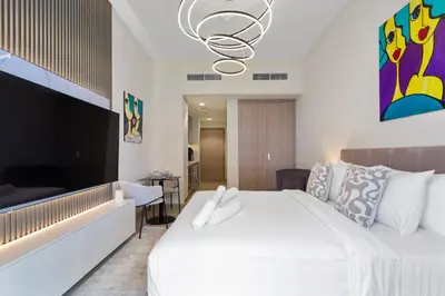 a bedroom with a large white bed and a living room at Sleek Studio Apartment in Azizi Riviera in Dubai