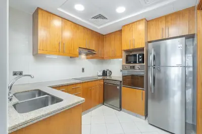 a kitchen with wooden cabinets and a stainless steel refrigerator at Premium 2 Bedroom in Trident Residence JBR in Dubai