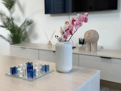 a white vase with pink flowers on a table at ASHRI HH Spacious Apartment in JVC, Binghatti Luna in Dubai