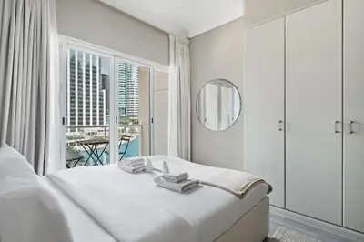 a white bedroom with a bed and a large window at Chic JLT Studio Lake View Metro 5min Marina in Dubai