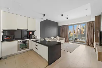 a kitchen with white cabinets and a living room at Burj Khalifa & Fountain From Your Balcony Near Dubai Mall & Metro in Dubai