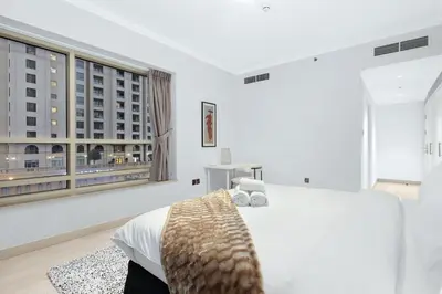 a white bedroom with a bed and a large window at Luxury 2BR Apartment Near JBR Beach with Pool and Gym Access in Dubai