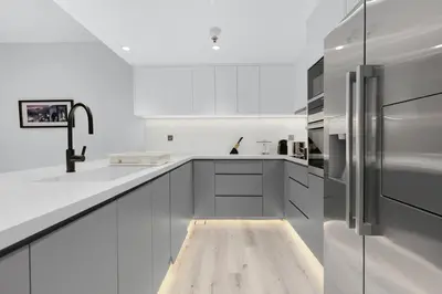 a kitchen with white cabinets and a wooden floor at Luxury 2BR Apartment Near JBR Beach with Pool and Gym Access in Dubai