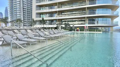 a pool of water with chairs in front of a building at Grand Bleu 02 - LIMITED OFFER! 1BR Coastal Retreat at Emaar Beachfront in Dubai