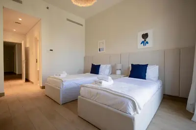 two beds in a white room with blue pillows at HiGuests - Experience Coastal Elegance at La Rive 2 in La Mer in Dubai