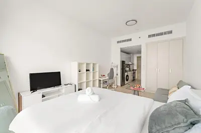 a white bedroom with a large bed and a tv at Chic JVC Studio in Dubai - Pool, Gym, Free Parking, City Views & Prime Location in Dubai