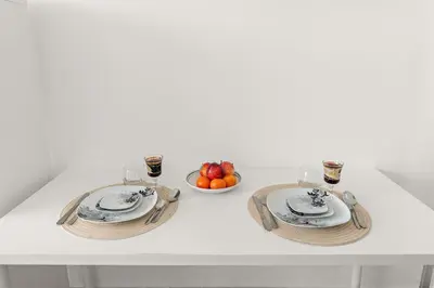 a white table with two plates and a bowl of fruit at Chic JVC Studio in Dubai - Pool, Gym, Free Parking, City Views & Prime Location in Dubai