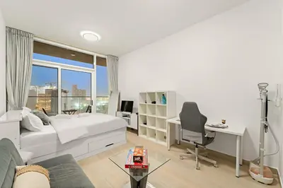 a bedroom with a bed and a desk and a window at Chic JVC Studio in Dubai - Pool, Gym, Free Parking, City Views & Prime Location in Dubai