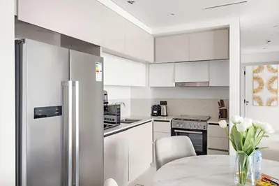a white kitchen with a table and a refrigerator at Silkhaus Seaside 2BDR in Marina Vista Beachfront in Dubai