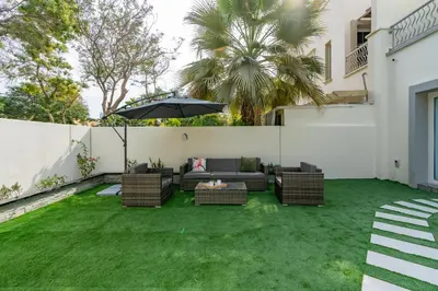 a patio with an umbrella and chairs and grass at White Sage Brand New 3BR Villa with Garden and Two Balconies in Dubai