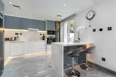 a kitchen with white cabinets and a counter with stools at White Sage Brand New 3BR Villa with Garden and Two Balconies in Dubai