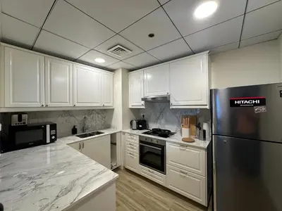 a kitchen with white cabinets and a stainless steel refrigerator at Luxe 2BR with Marina View in JBR and Walk to the Beach in Dubai