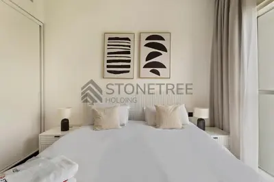 a white bedroom with a large white bed with two lamps at Cozy 1BR at Collective Tower 1 Near Hills Mall in Dubai