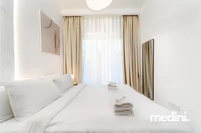 a white bed in a white bedroom with a window at 10 min from Burj Khalifa - Sauna - Gym - Damac Reva in Dubai