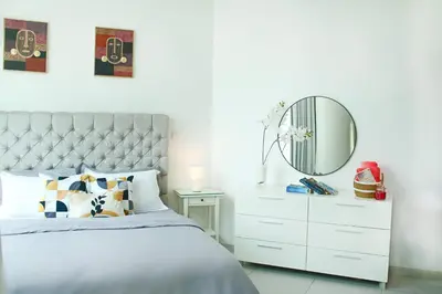 a white bedroom with a white dresser and a mirror at 2 Bedroom Apartment with Spacious Private Garden in Dubai Marina in Dubai