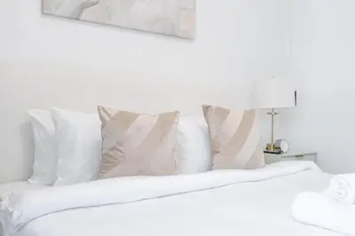 a white bed with white pillows and a lamp at StayShort - Bright and Airy 1-Bedroom Apartment Perfect for 4 in Dubai Marina in Dubai