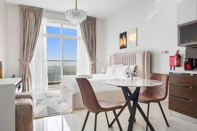 a white bedroom with a bed and a table and chairs at Lux Studio Apt near Butterfly Garden - Pool & Gym in Dubai