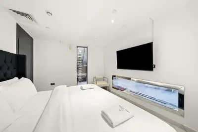 a bedroom with a white bed with a flat screen tv at Elegant 2BR with Burj Views, Pool, Gym, and Quick Metro Access in Dubai