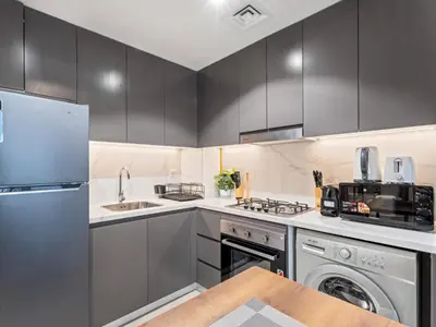 a kitchen with gray cabinets and a washer and dryer at Cozy Stay 1BR in Azizi Pearl in Dubai