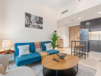 a living room with a blue couch and a table at Cozy Stay 1BR in Azizi Pearl in Dubai