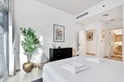 a white bedroom with a bed and a plant at Stylish 1BR APT with Gym, Pool & Private Parking in Dubai