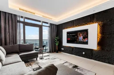 a living room with a couch and a tv on a wall at Sky-High 2BR - Infinity Pool & Burj Khalifa Views in Dubai