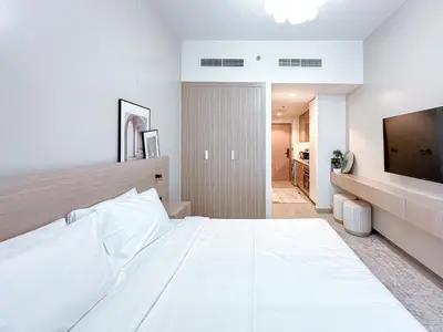 a white bedroom with a large bed and a flat screen tv at Cozy Studio in Azizi Riviera with Balcony in Meydan City in Dubai