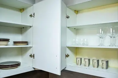 a white kitchen with plates and glasses on shelves at Modern Studio in Discovery Gardens, Close to Metro in Dubai