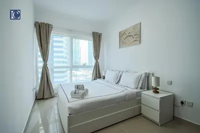 a white bedroom with a bed and a window at Cozy 1-Bedroom Apartment in N2 Lakepoint Tower JLT in Dubai