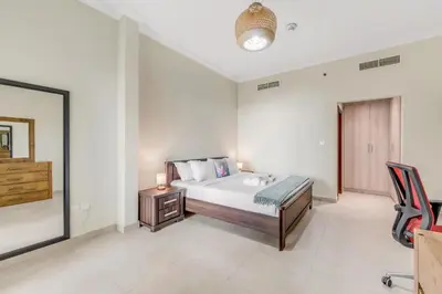 a bedroom with a bed and a desk and a chair at Waves - Spacious 1BR with Balcony & Cozy Interiors in JVC in Dubai