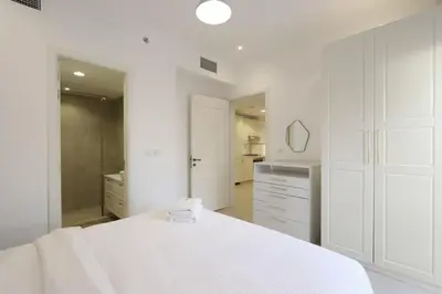 a white bedroom with a large bed and a bathroom at Livbnb-Modern 1BR Oasis with Stunning Terrace, JVC in Dubai