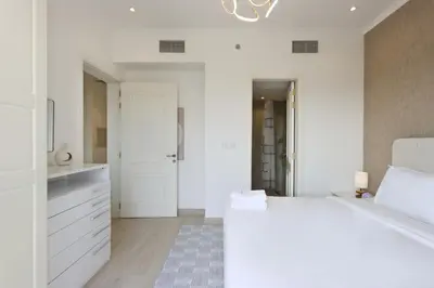 a white bedroom with a large bed and a hallway at Livbnb - Homey 1B with Spacious Terrace in District 14, JVC in Dubai
